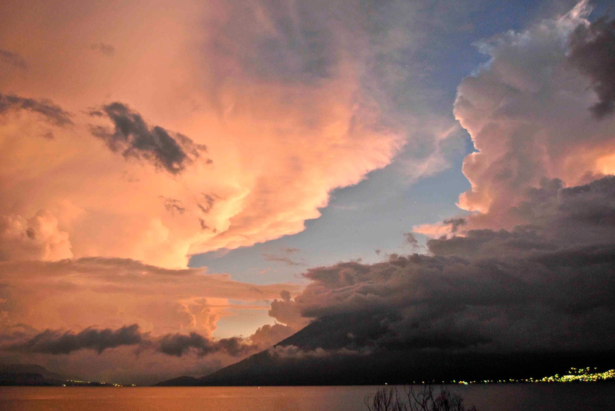 Pink dusk clouds above the volcanoes, village lights coming on across the water